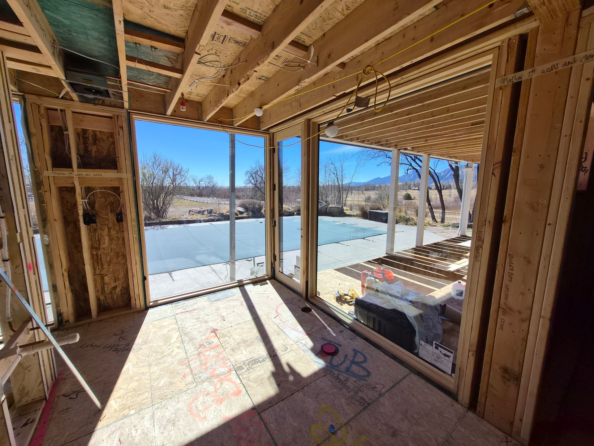 Interior view of a residential construction site looking out through large glass sliding doors onto a concrete patio.