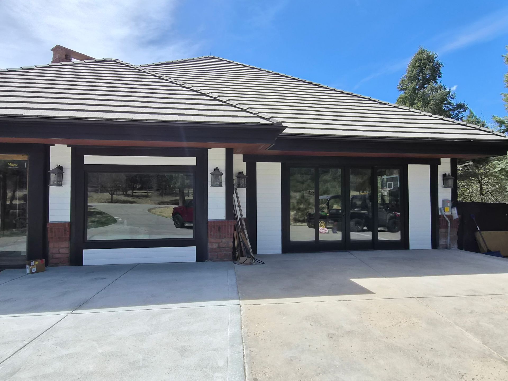 A suburban home with white stucco walls, dark brown trim, a tiled roof, and two large glass garage-style doors.