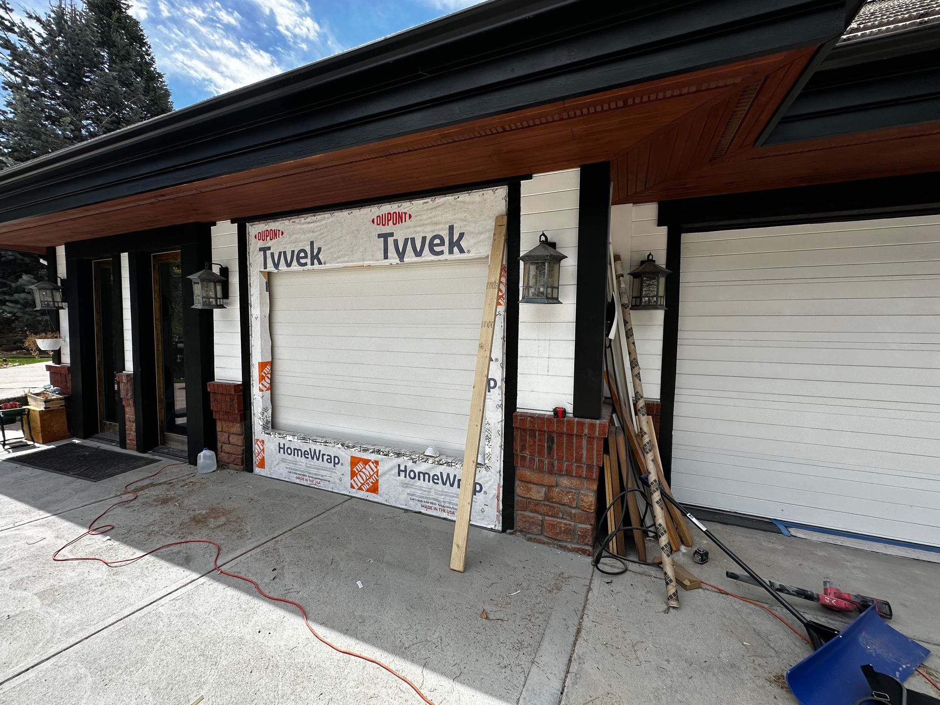 A partially renovated house exterior featuring horizontal white siding, brick accents, black trim, and Tyvek house wrap.