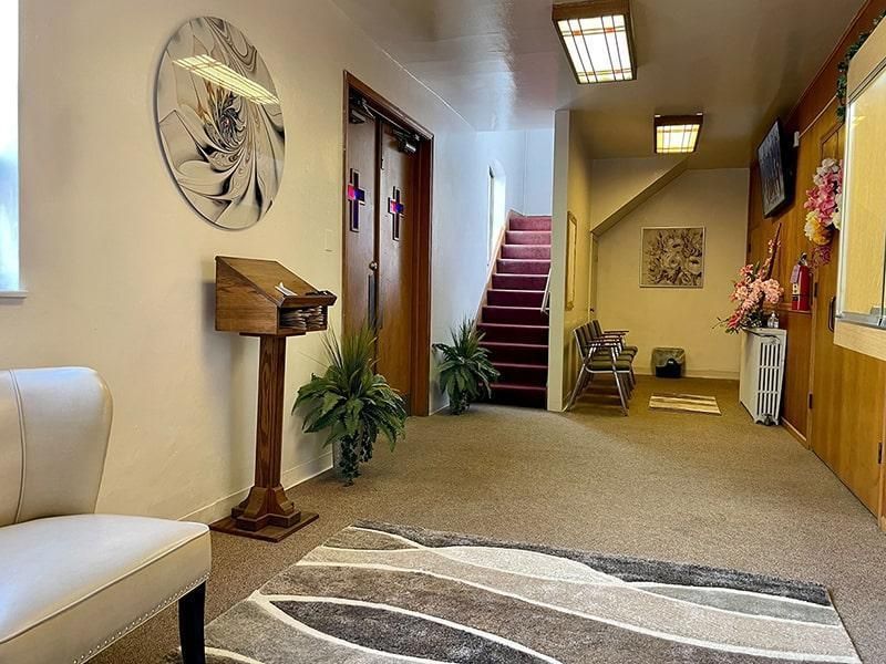 Church hallway with stairs, pew, floral arrangements, and decorative circular art.
