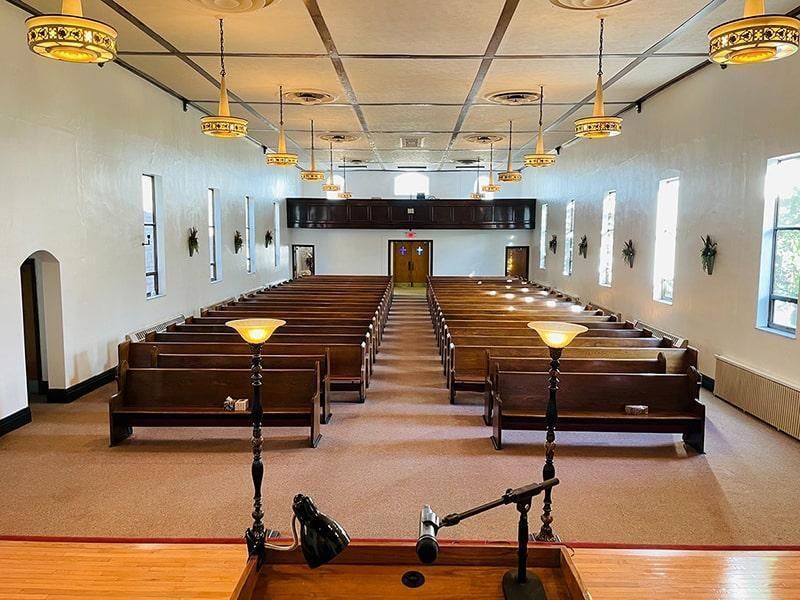 Interior view of a church sanctuary with rows of pews, a pulpit, and overhead lighting.