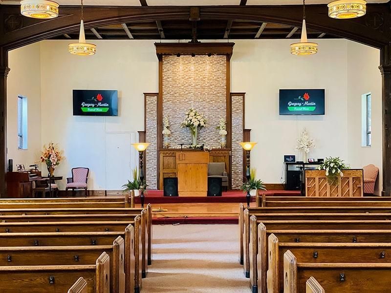 Interior of a church sanctuary, featuring pews, pulpit, altar, and two screens displaying text, lit by hanging chandeliers.