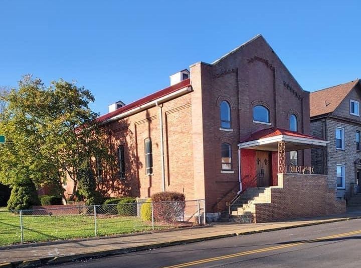 Red brick church with red roof and arched windows. Front porch with steps.