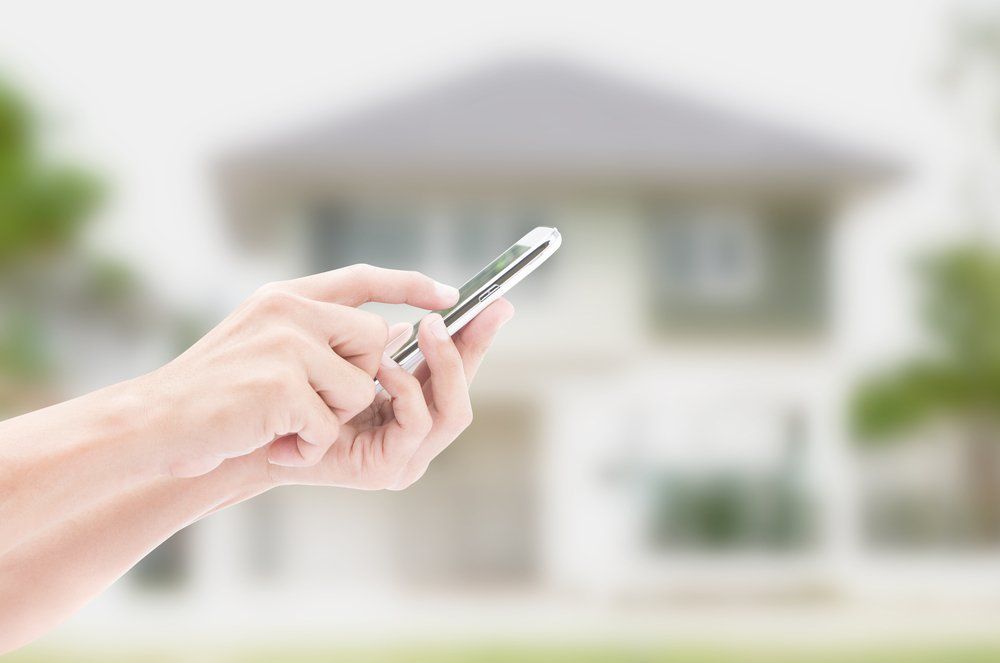 A person is holding a cell phone in front of a house.