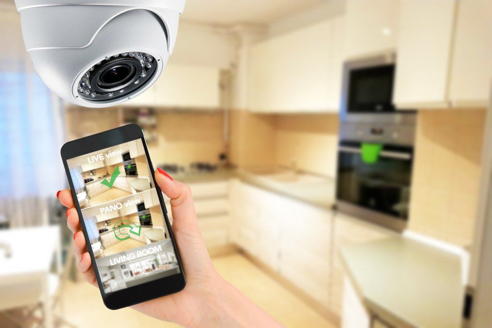 A person is holding a cell phone in front of a security camera in a kitchen.
