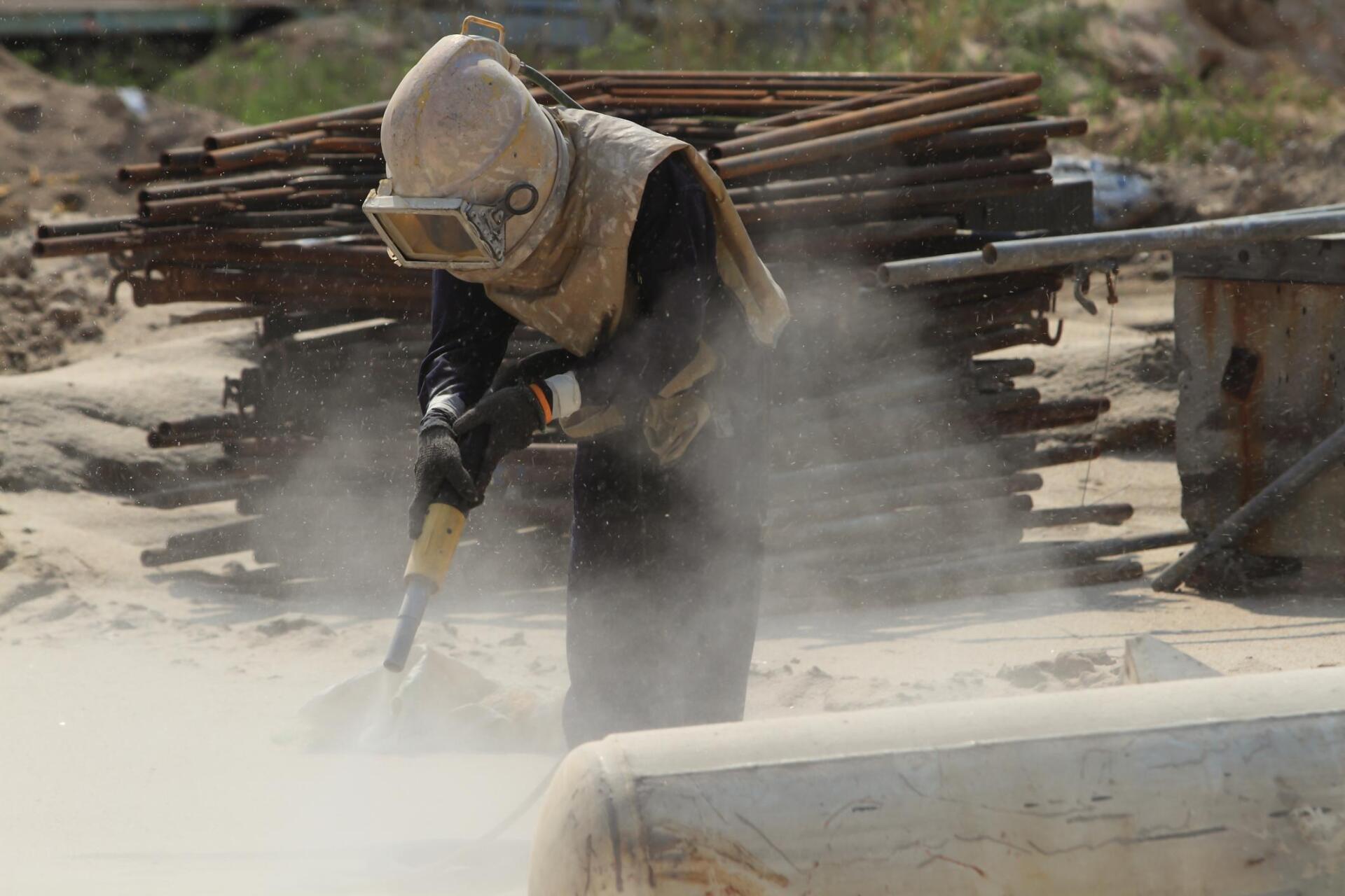 worker sandblasting the sand