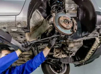 Mecânico trabalhando embaixo de um carro, removendo a roda e o conjunto do freio em uma oficina mecânica.