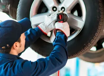 Mecânico apertando uma porca de roda de um carro com uma ferramenta elétrica.