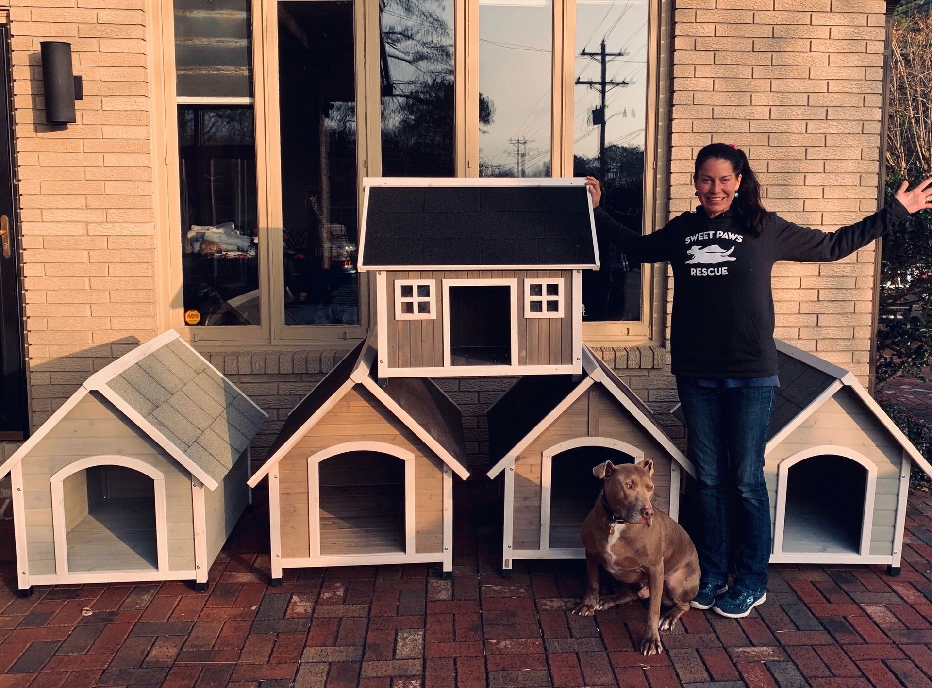 A person standing on a brick patio with four wooden dog houses of various styles, accompanied by a medium-sized dog.