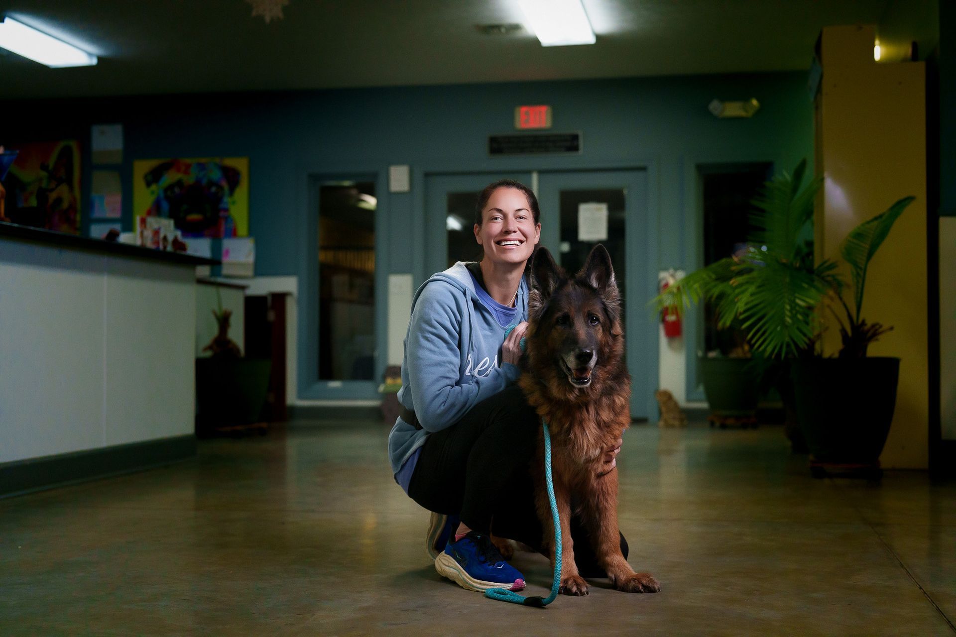 Woman with arms outstretched, standing near five doghouses. Dog sits in front.