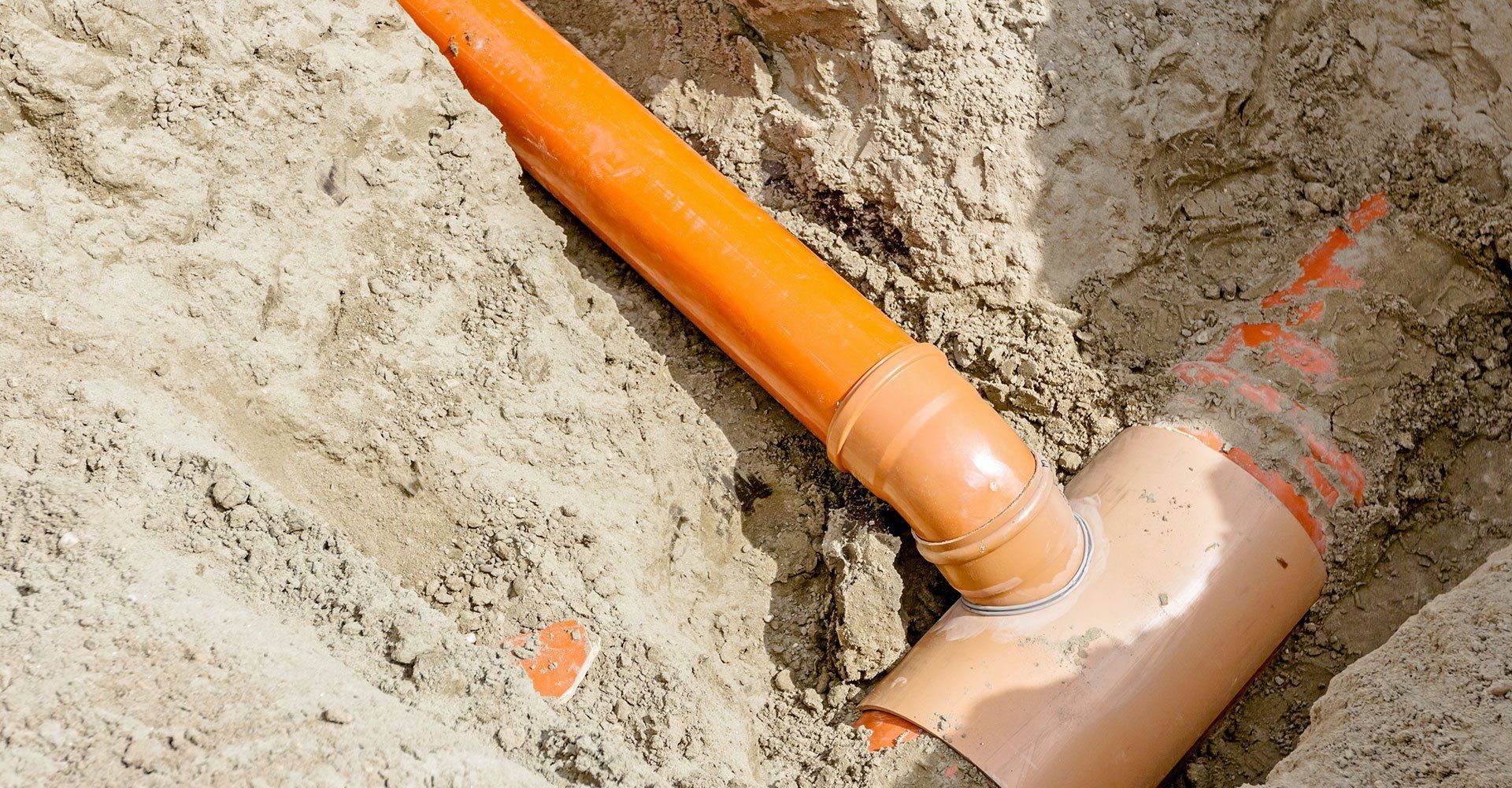 Orange PVC pipes joined in a sand-filled trench.