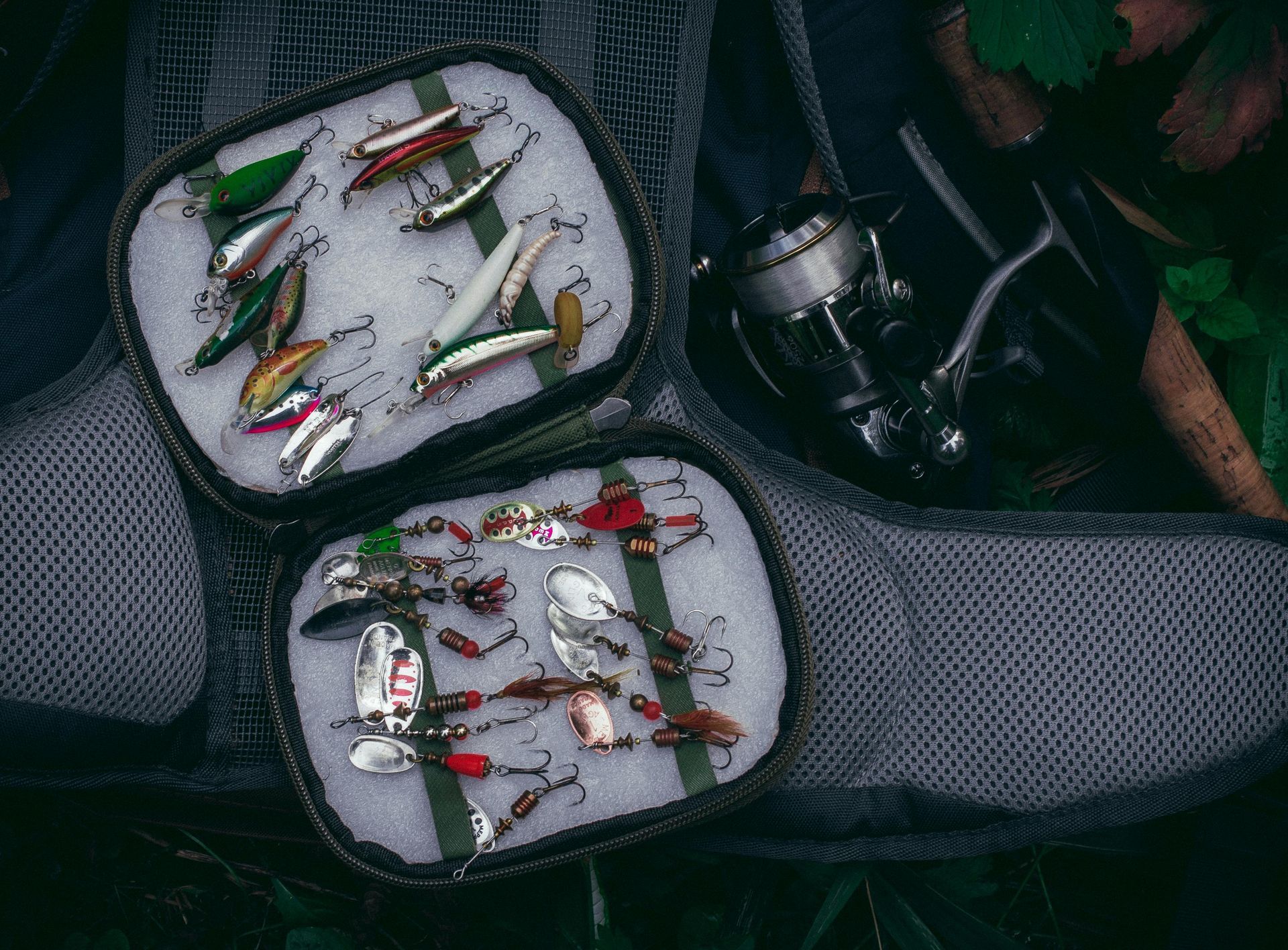 Tray of colorful fishing lures arranged on dark fabric, with a fishing rod and reel nearby.
