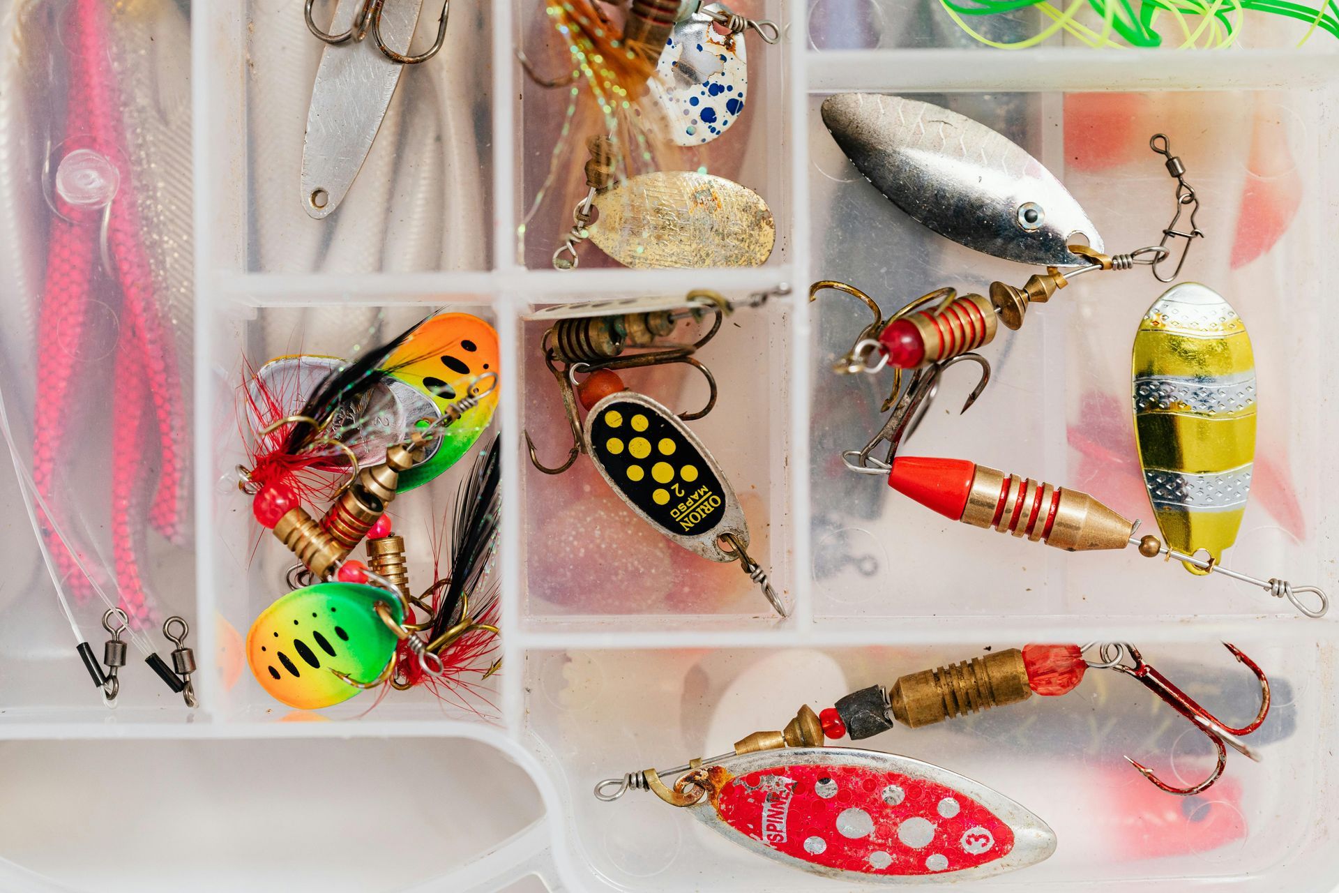 Assorted colorful fishing lures and tackle arranged in a compartmented plastic organizer.