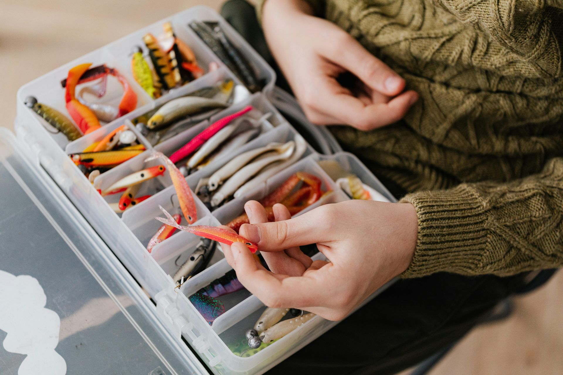 Hands organizing colorful fishing lures in a tackle box on a table
