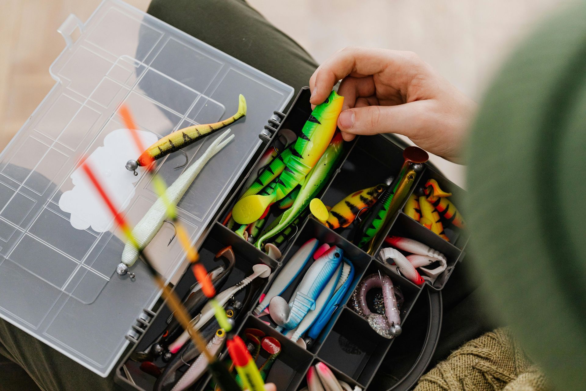 Person holding an open tackle box with colorful fishing lures and hooks.