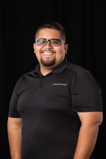 Smiling man in glasses wearing a black polo shirt against a dark background