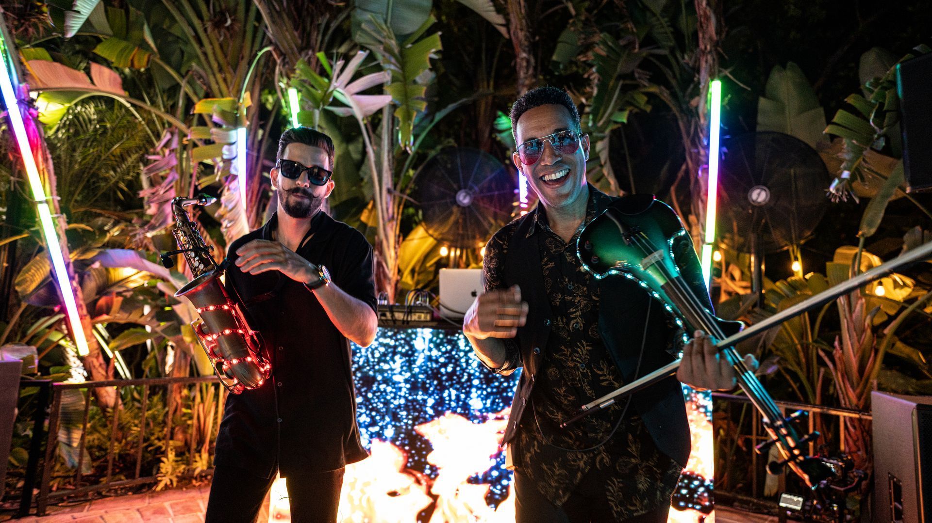 Two smiling people holding glowing LED batons at a nighttime outdoor festival
