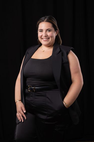 Smiling woman in a black outfit standing against a dark studio backdrop