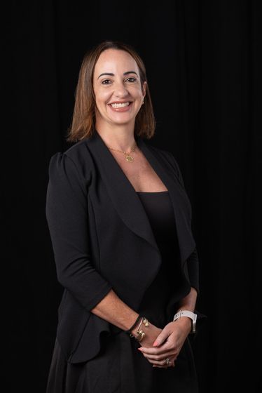Smiling woman in a black blazer posing against a dark background.