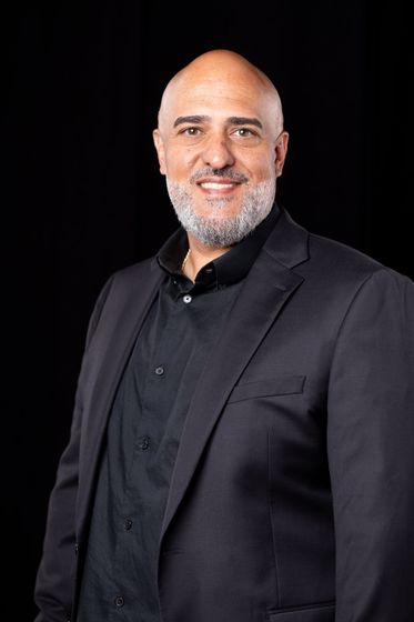 Smiling bald man in a black suit and shirt against a black background