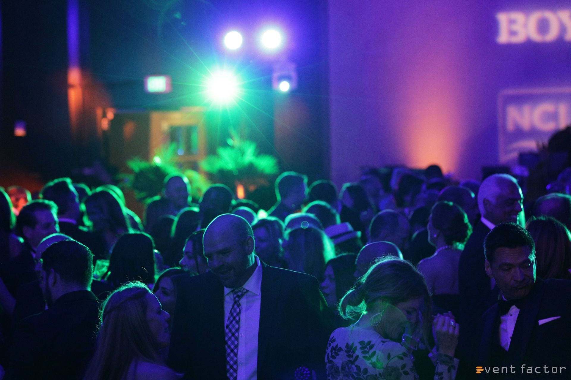 Crowded nightclub with people dancing under colorful green and purple lights