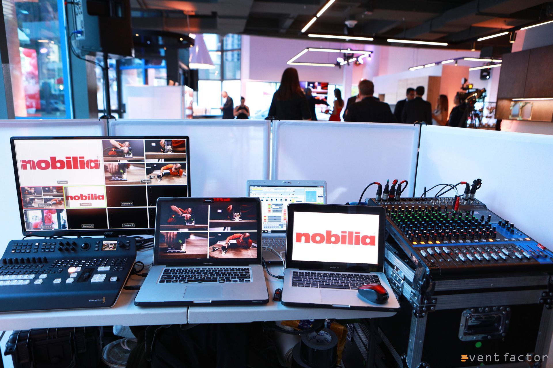 Live event production desk with monitors, audio consoles, and laptops displaying “nobilia” branding