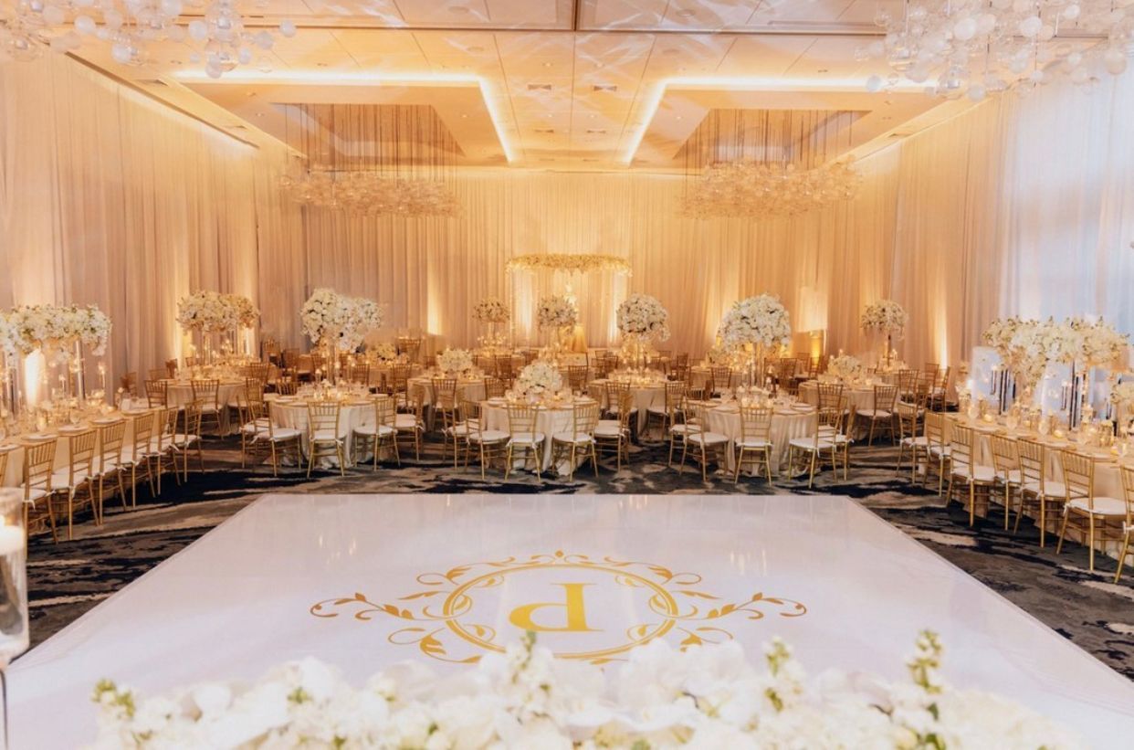 Elegant wedding reception hall with gold decor, floral centerpieces, chandeliers, and a checkered dance floor