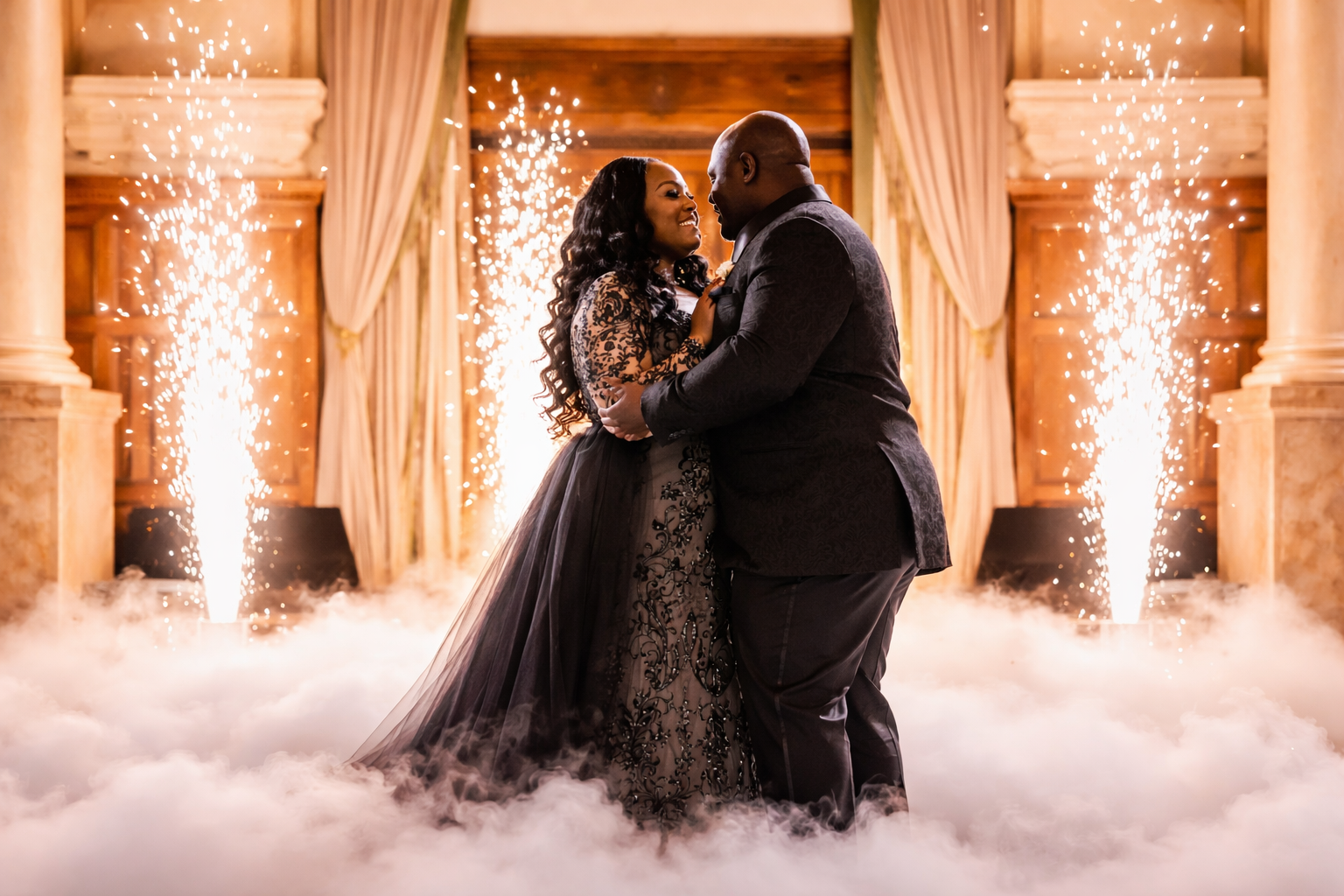 Couple embracing in a fog-filled ballroom with sparkling gold fountains and draped curtains