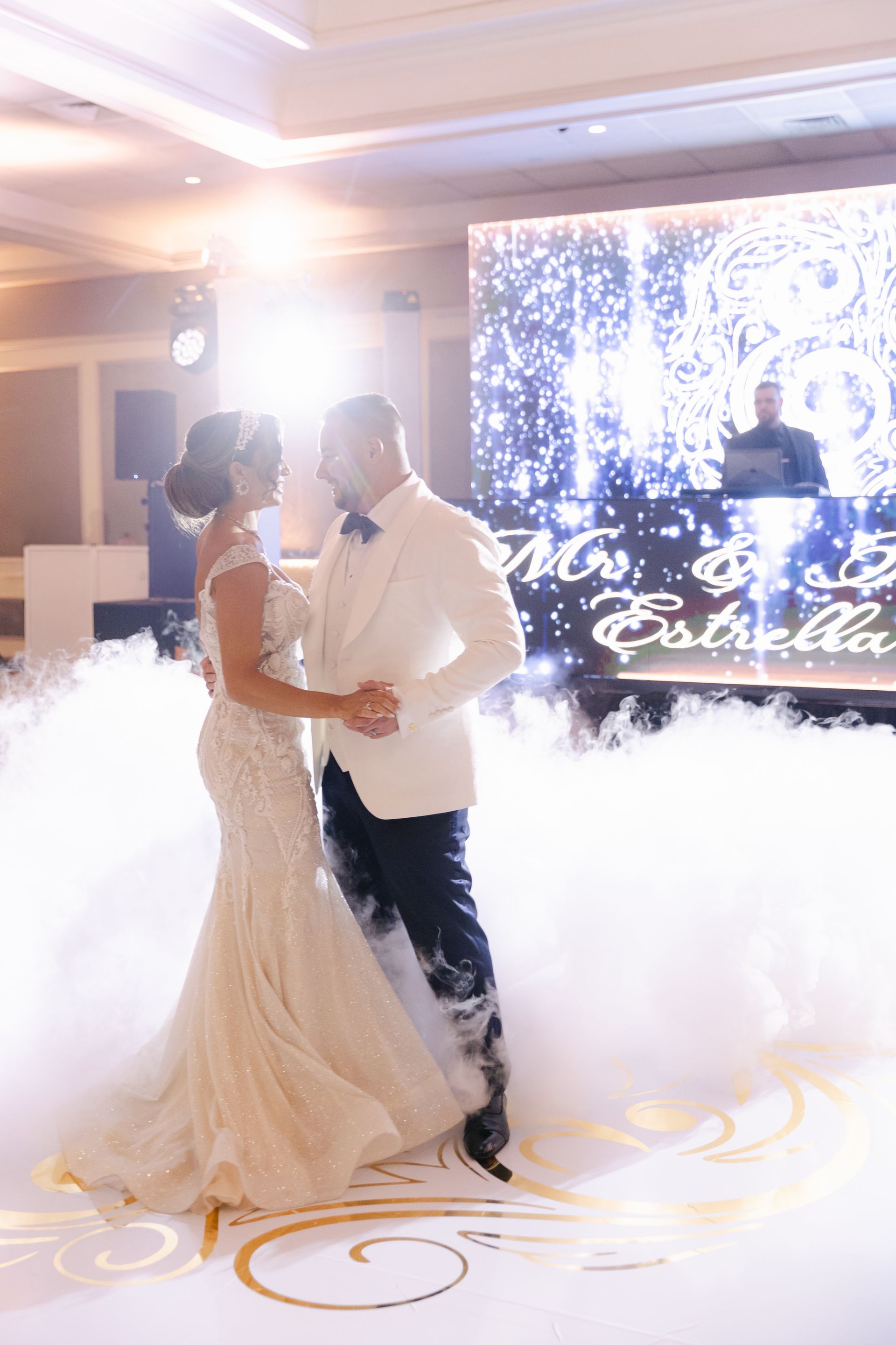 Newlyweds walk through sparklers and fog at a wedding reception, holding hands under warm lights
