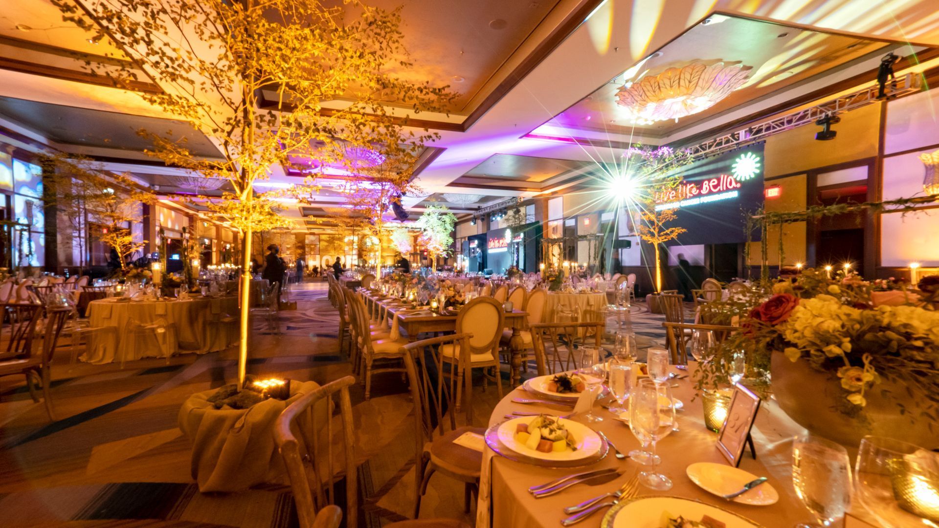 Elegant banquet hall with round tables, floral centerpieces, and warm golden lighting.