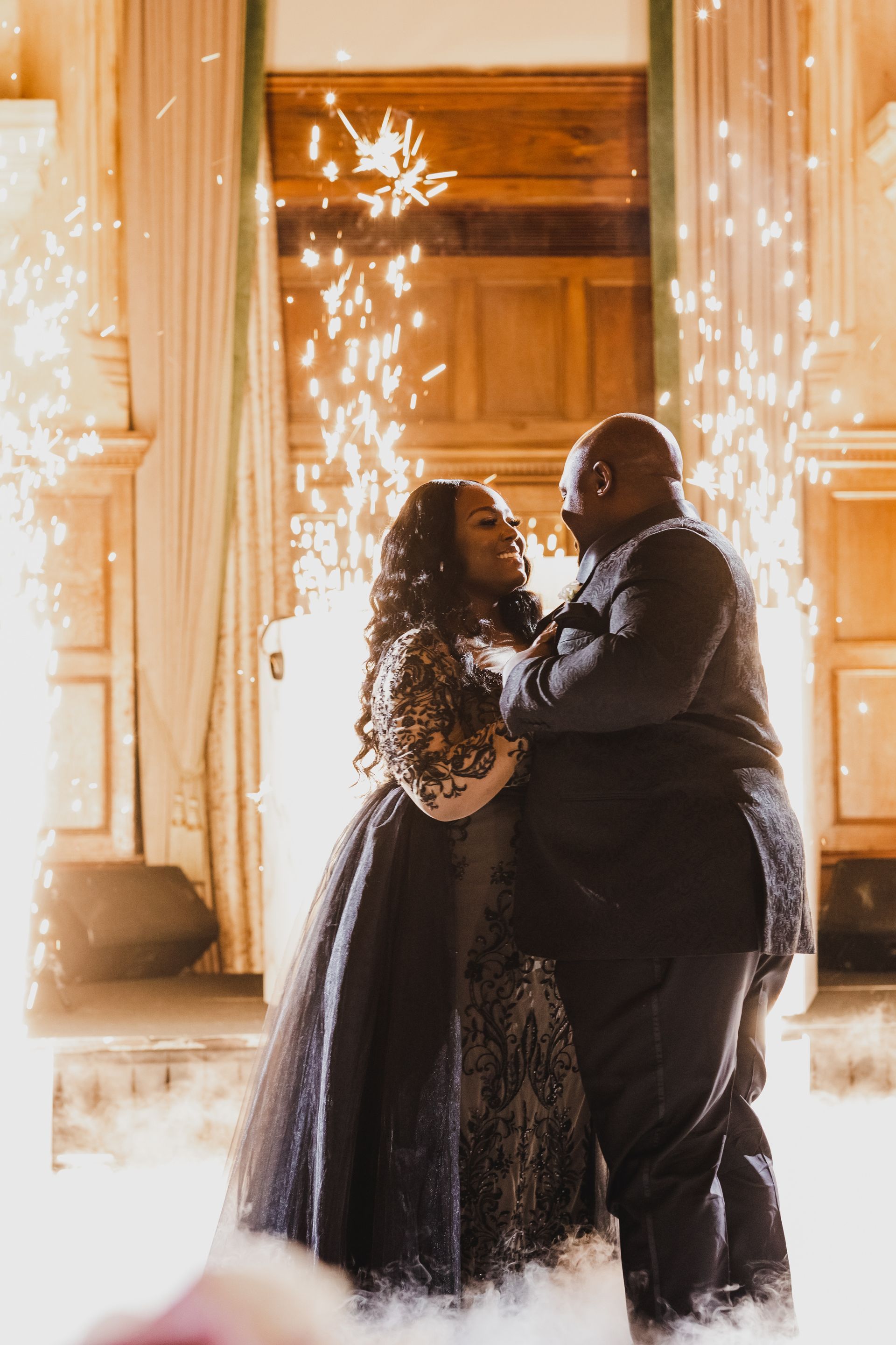 Couple embracing in a glowing, spark-filled ballroom surrounded by low-lying fog
