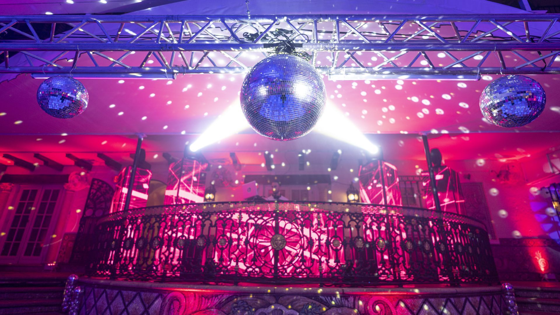 Disco-lit nightclub with mirrored balls, pink and purple lights, and a balcony railing