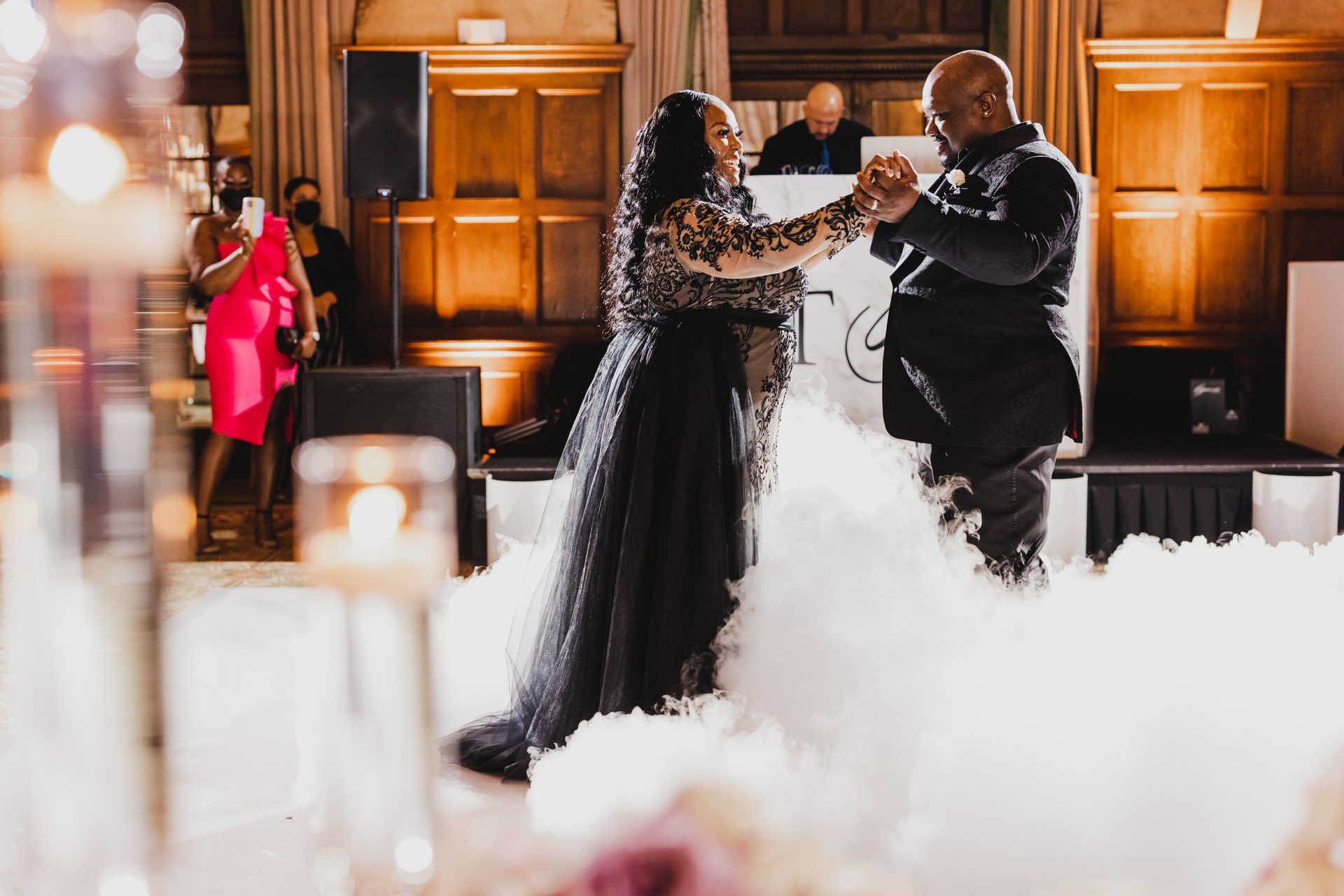 Couple embracing in formal attire amid indoor sparklers and low-lying fog at a decorated venue