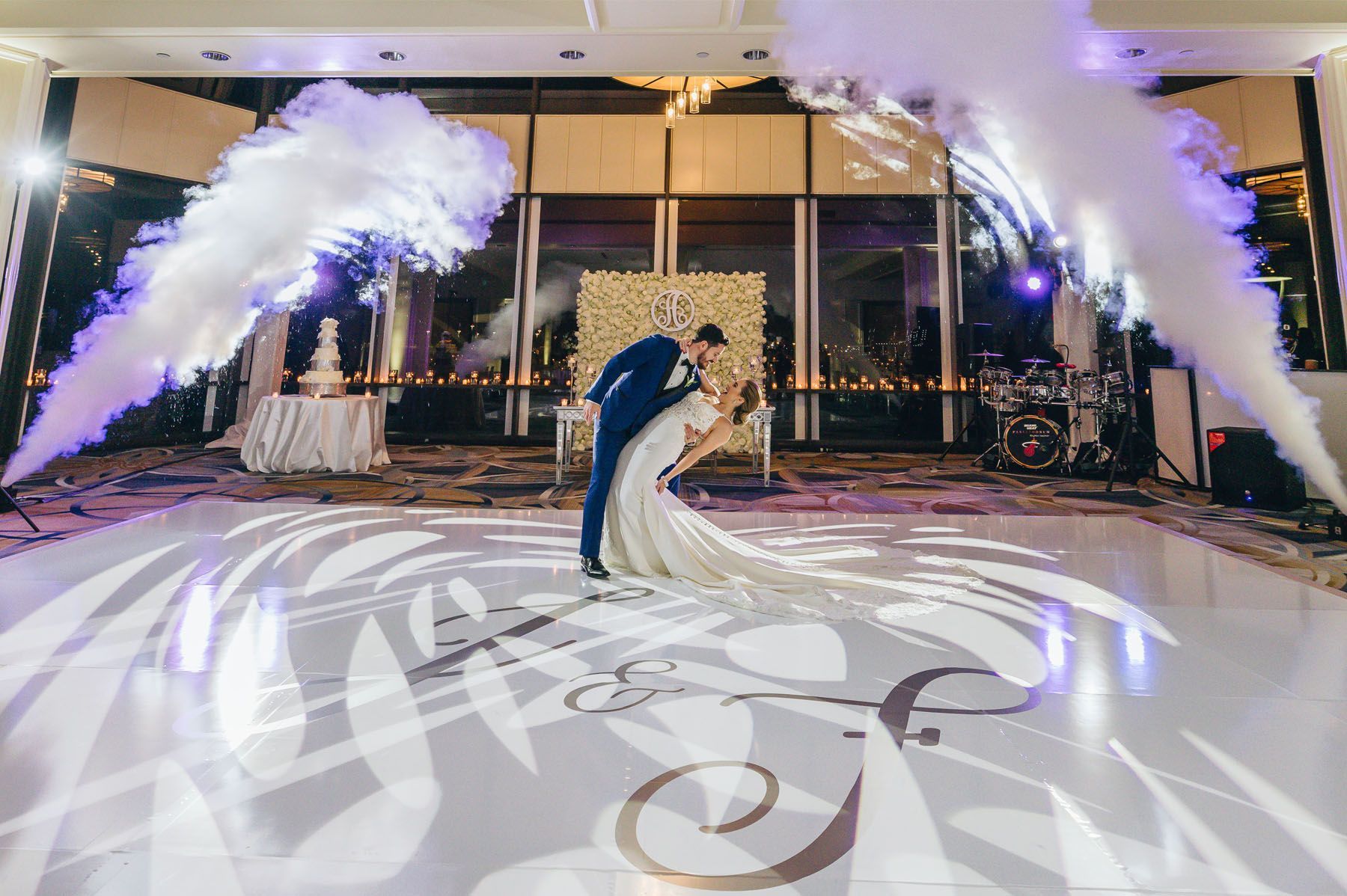 Bride and groom kiss on a lit dance floor with white smoke effects at an elegant indoor reception