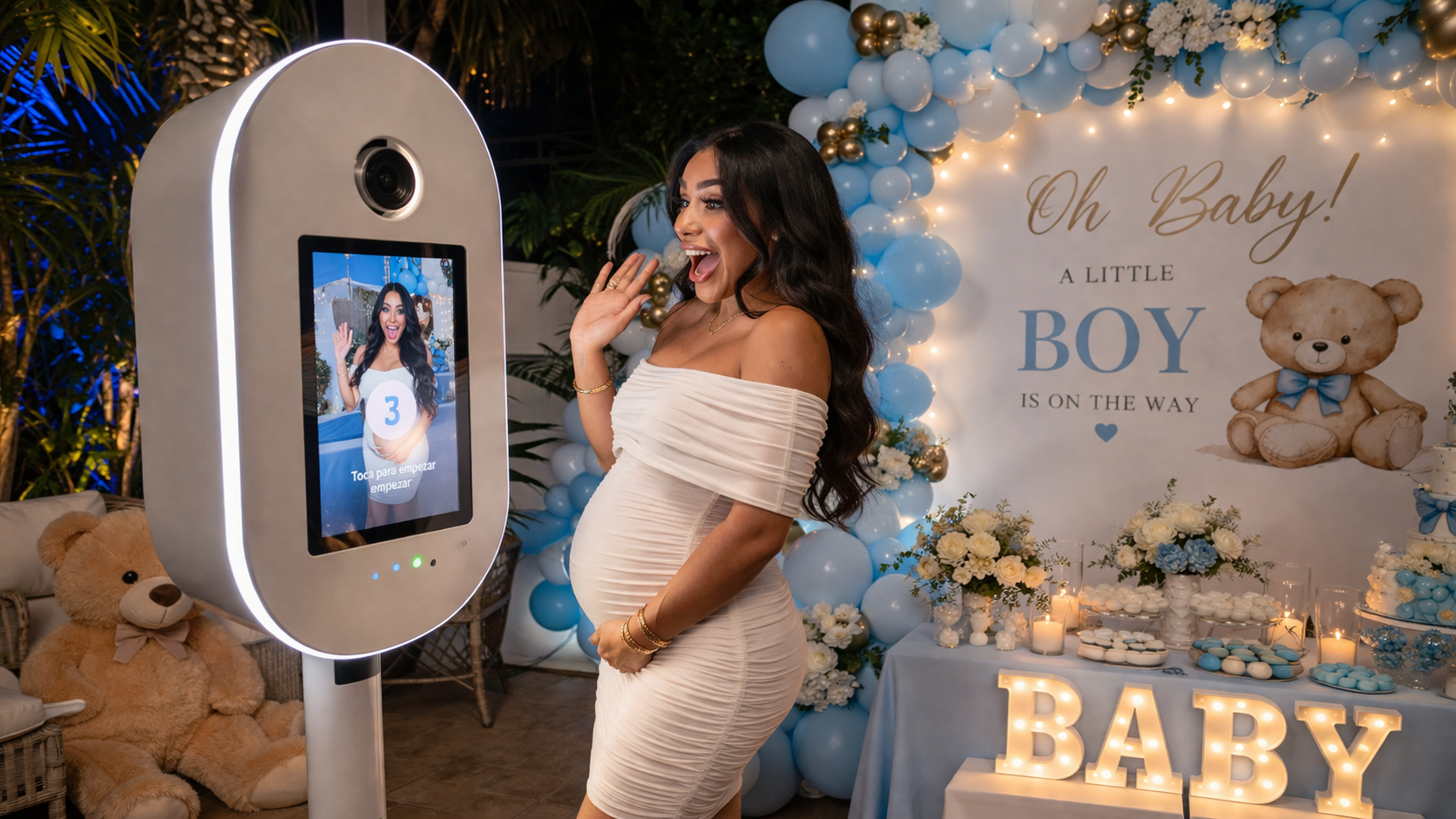 Pregnant woman in a white dress posing beside a baby shower photo booth with blue balloons and “Oh Baby!” decor
