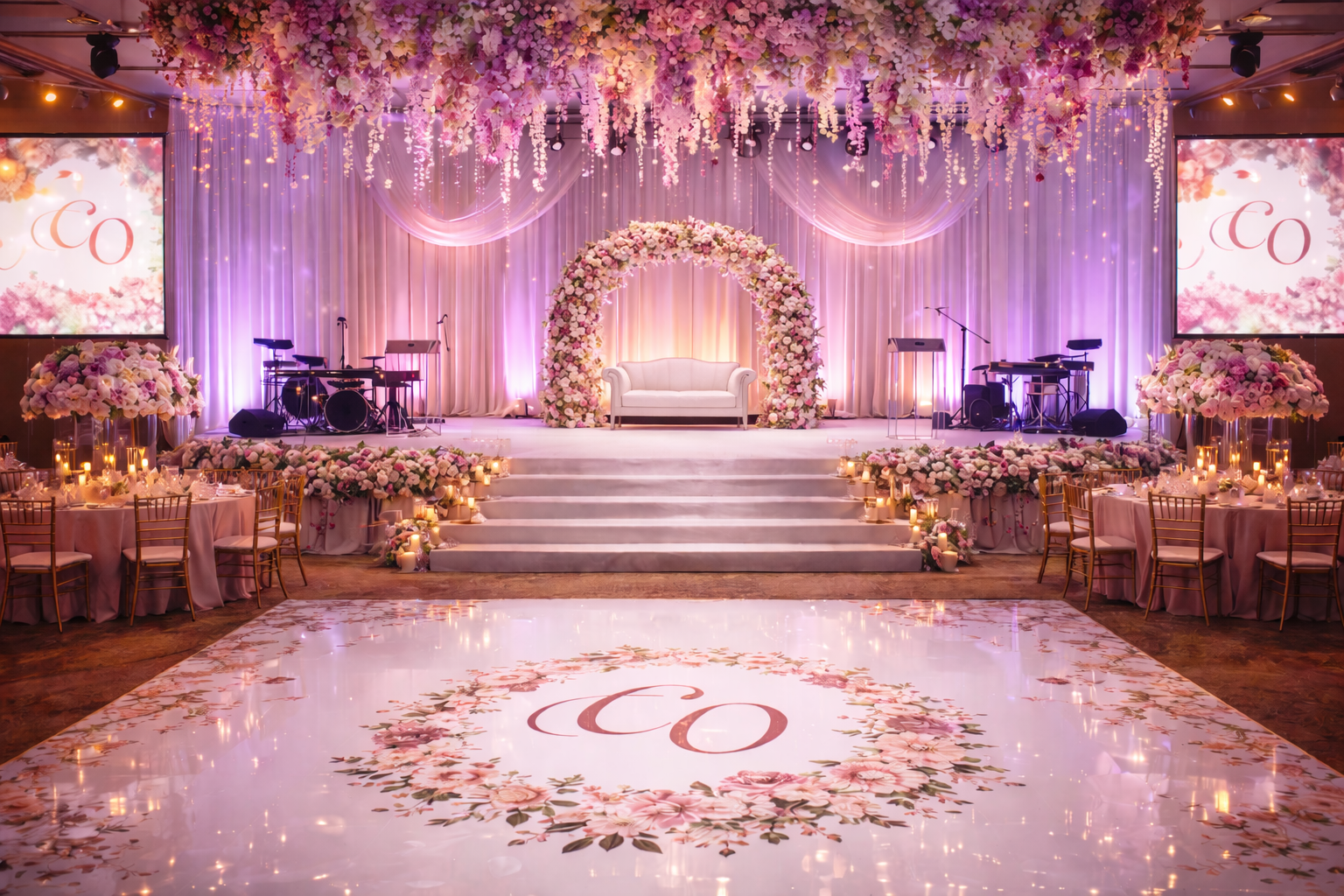Lavishly decorated wedding stage with floral arch, pink-purple lighting, and monogrammed dance floor