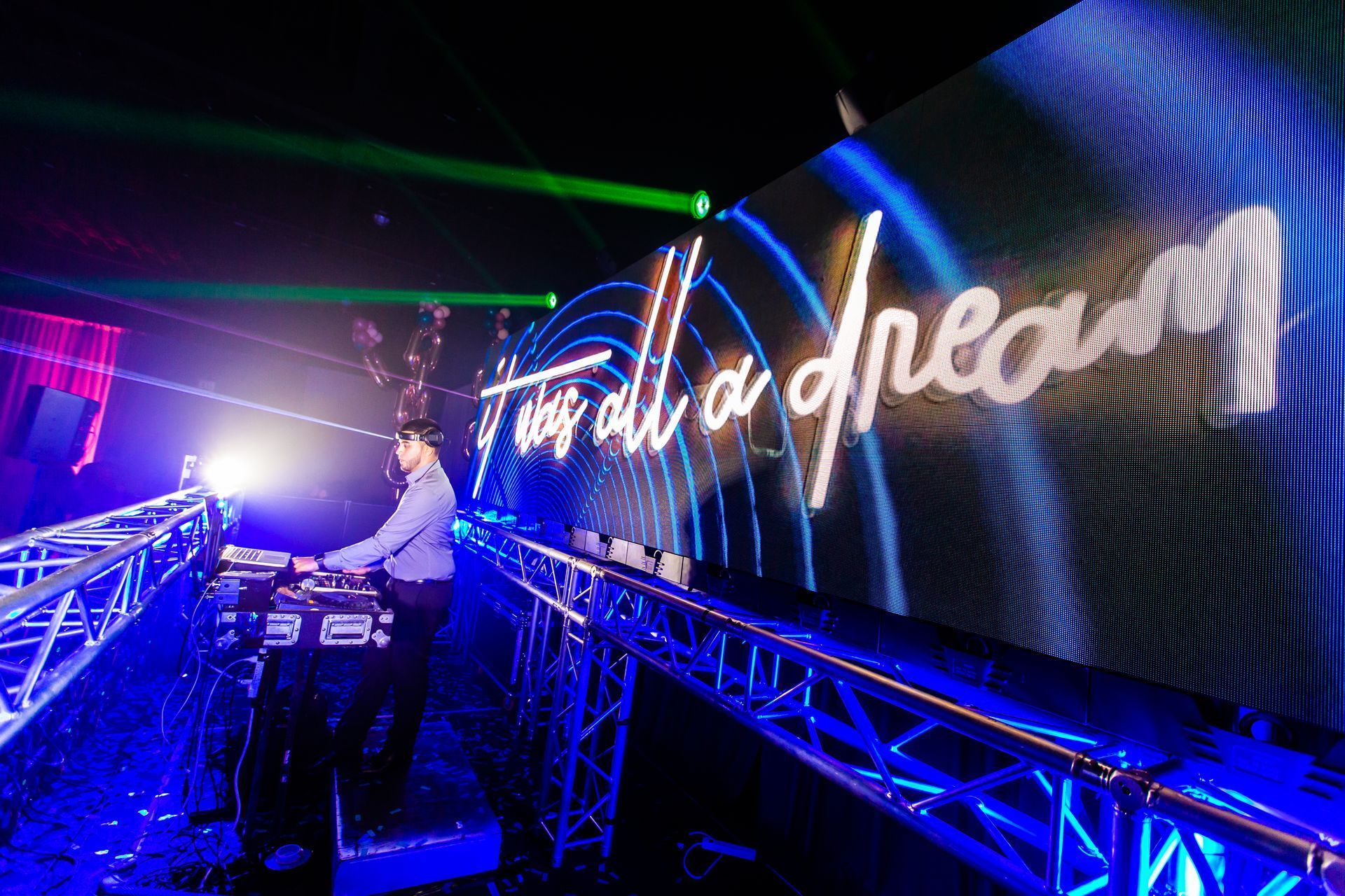 DJ performing at a nightclub stage with blue neon lights and a large glowing “end of the line” sign