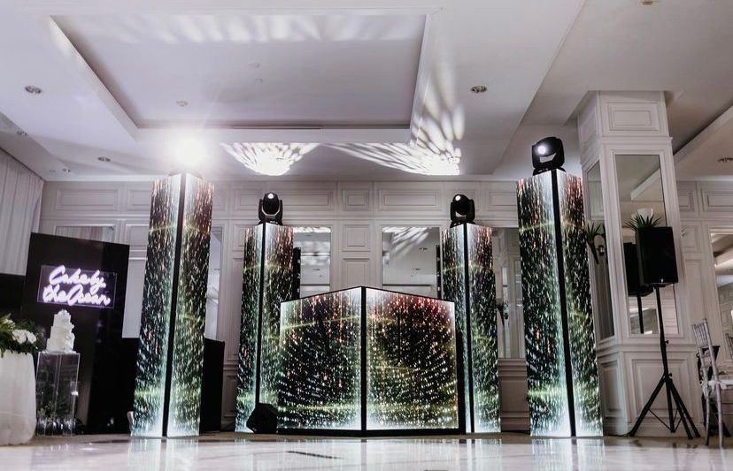 Elegant event hall with white decor, illuminated floral panels, and a central mirrored backdrop on a glossy floor