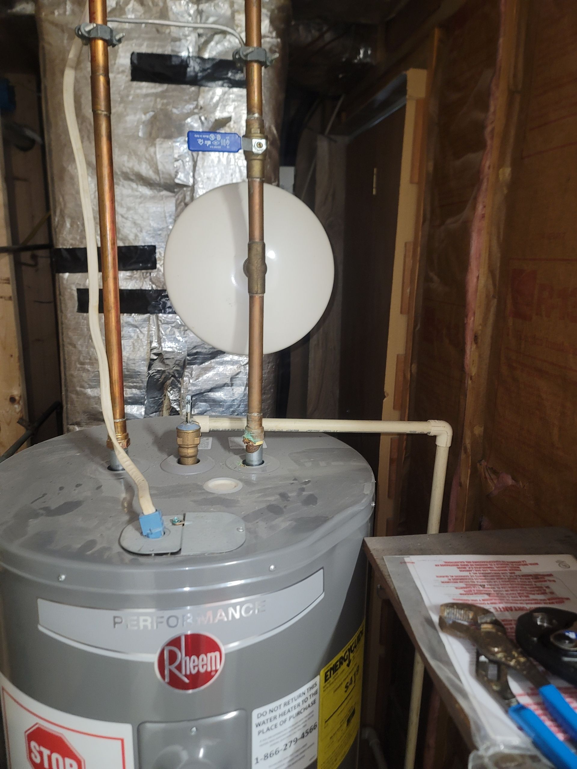 Water heater with attached expansion tank and copper pipes, in a utility room.