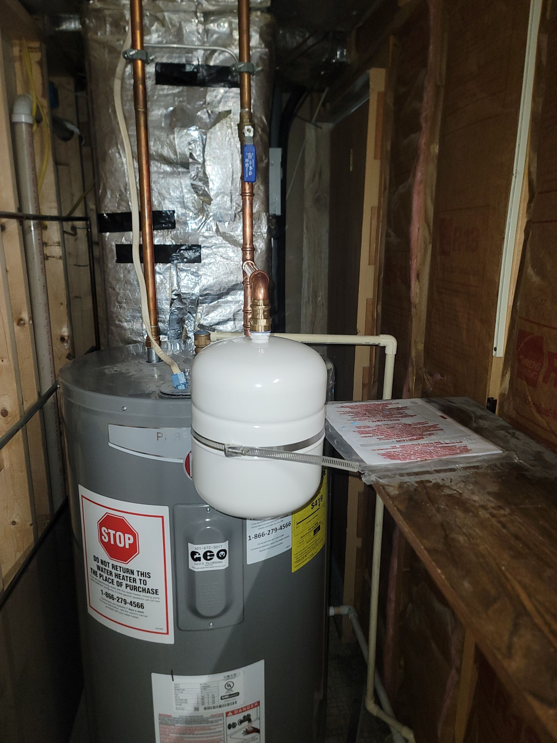 A water heater in a wooden framed enclosure with a white expansion tank.