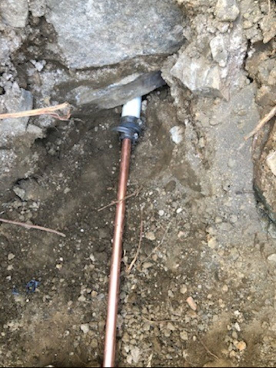 Copper water pipe connected to white plastic pipe, underground in dirt.