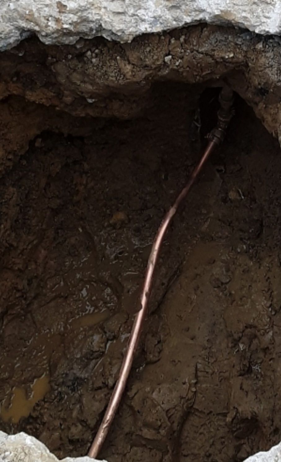 Copper pipe in a dirt-filled excavation.