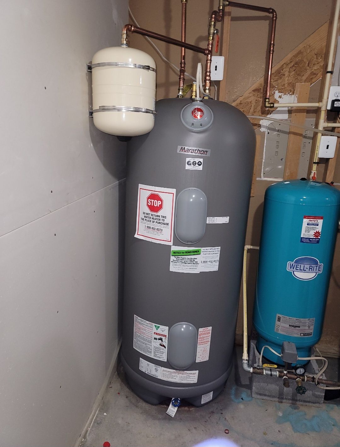 Water heater with expansion tank and a blue pressure tank in a utility room.