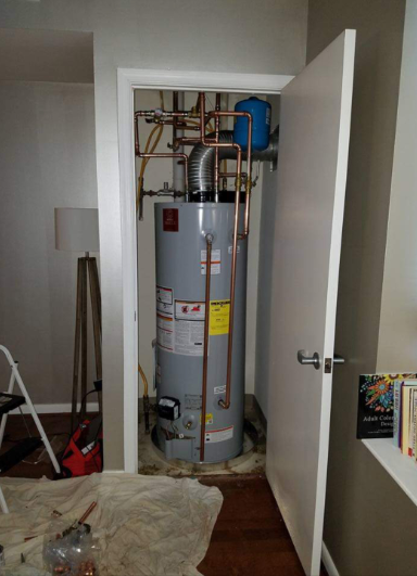 A water heater is sitting in a closet next to a door.