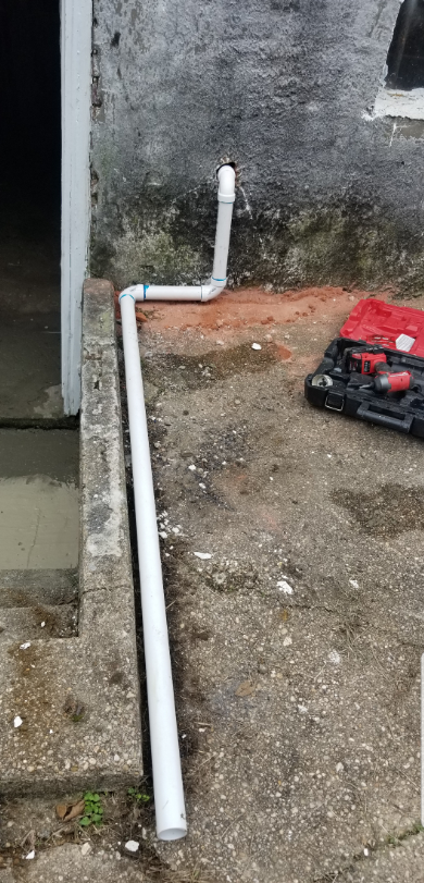 A white pipe is sitting on the ground next to a wall.