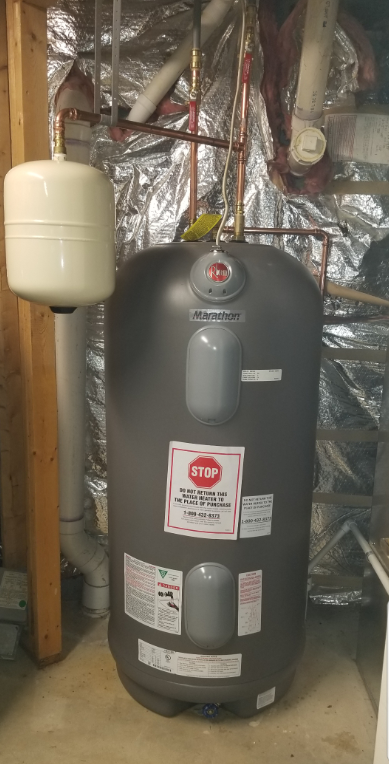 A large water heater is sitting in a basement next to a wall.