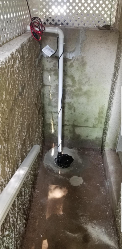 A sump pump is installed in a basement next to a staircase.