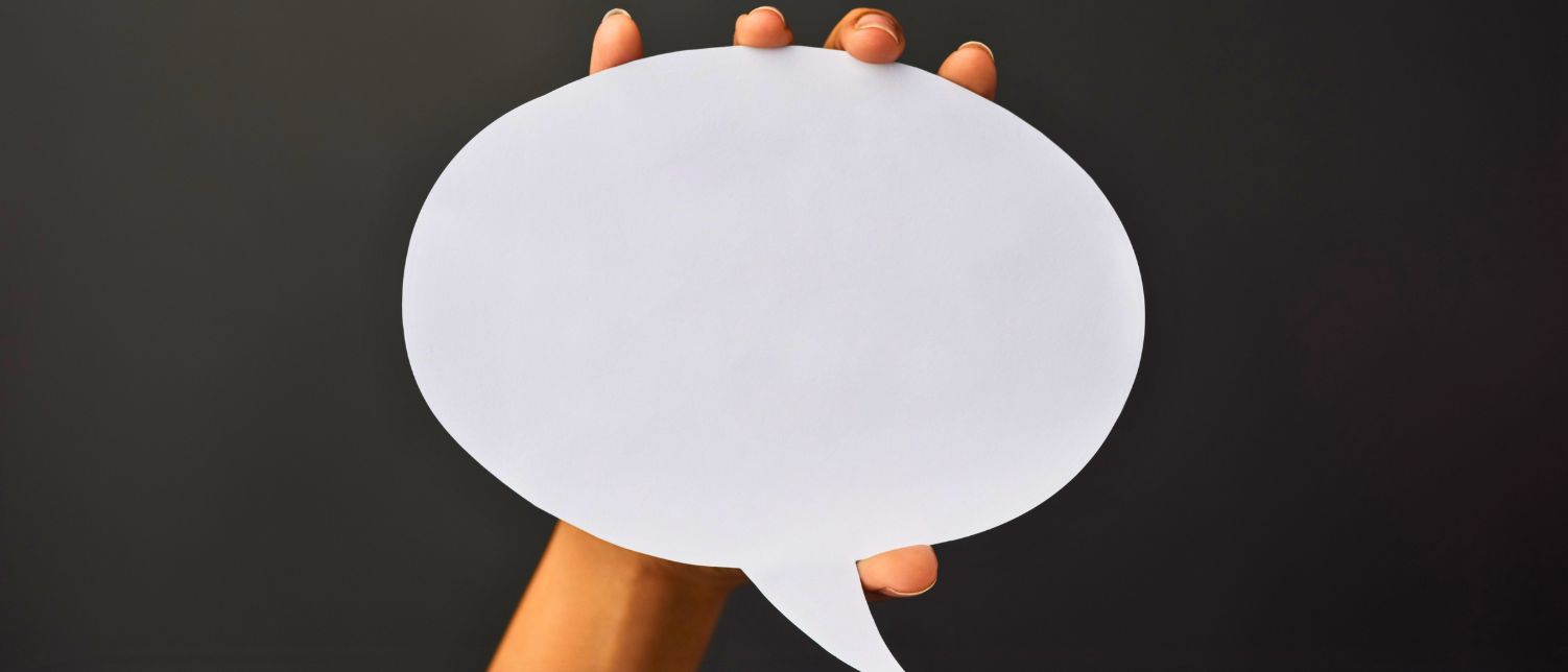 Hand holding a white speech bubble against a dark gray background.