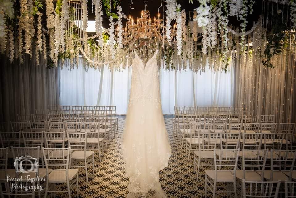 A wedding dress is hanging from the ceiling in front of a row of chairs.