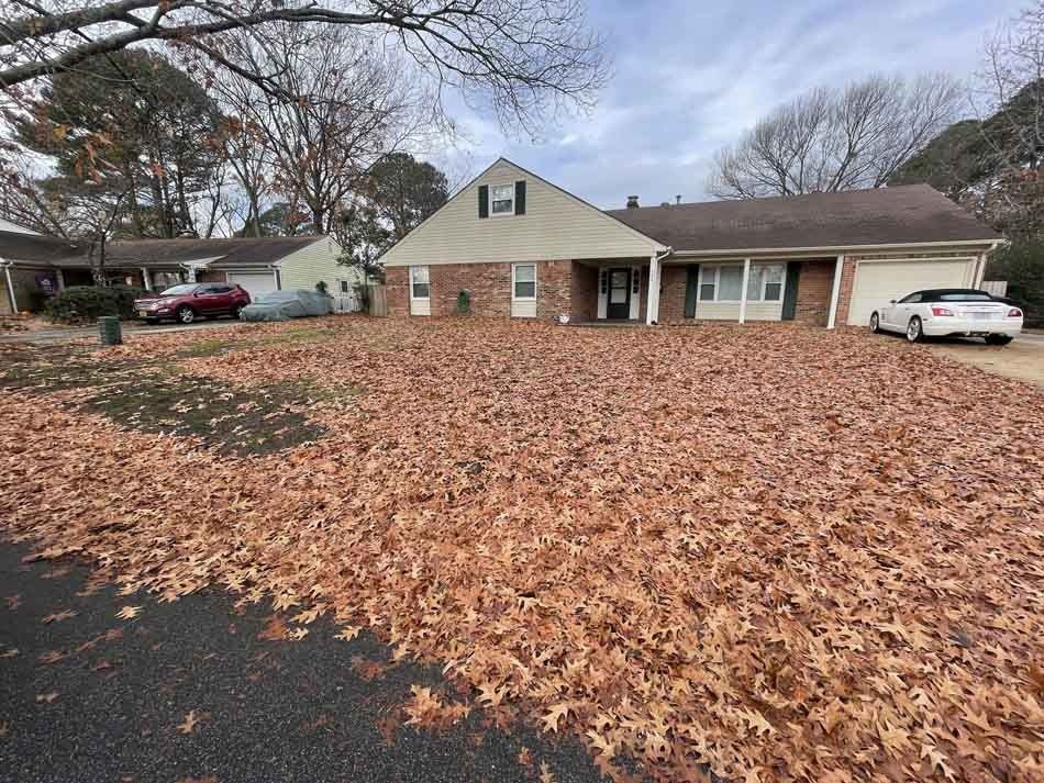 A suburban home covered in fallen brown leaves. A car is parked in the driveway.